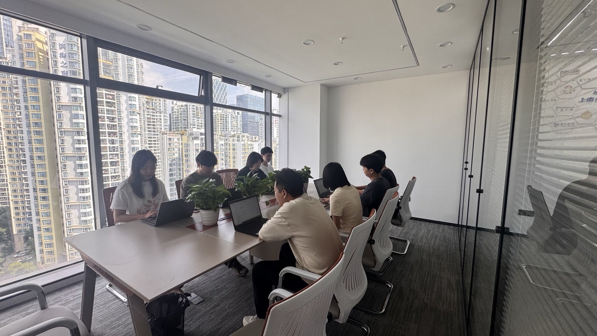 九序团队围坐在会议室长桌前讨论方案,窗外是城市景观